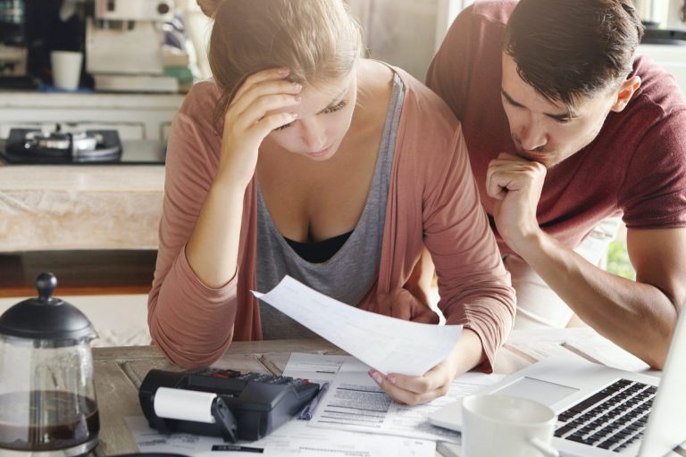 Young couple calculating their domestic budget together in kitchen, trying to save money for buying